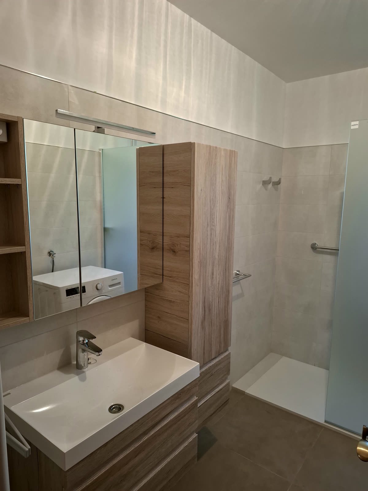 Dokončana kopalnica z odprtim tušem, hrastovo omarico in lučjo nad ogledalom